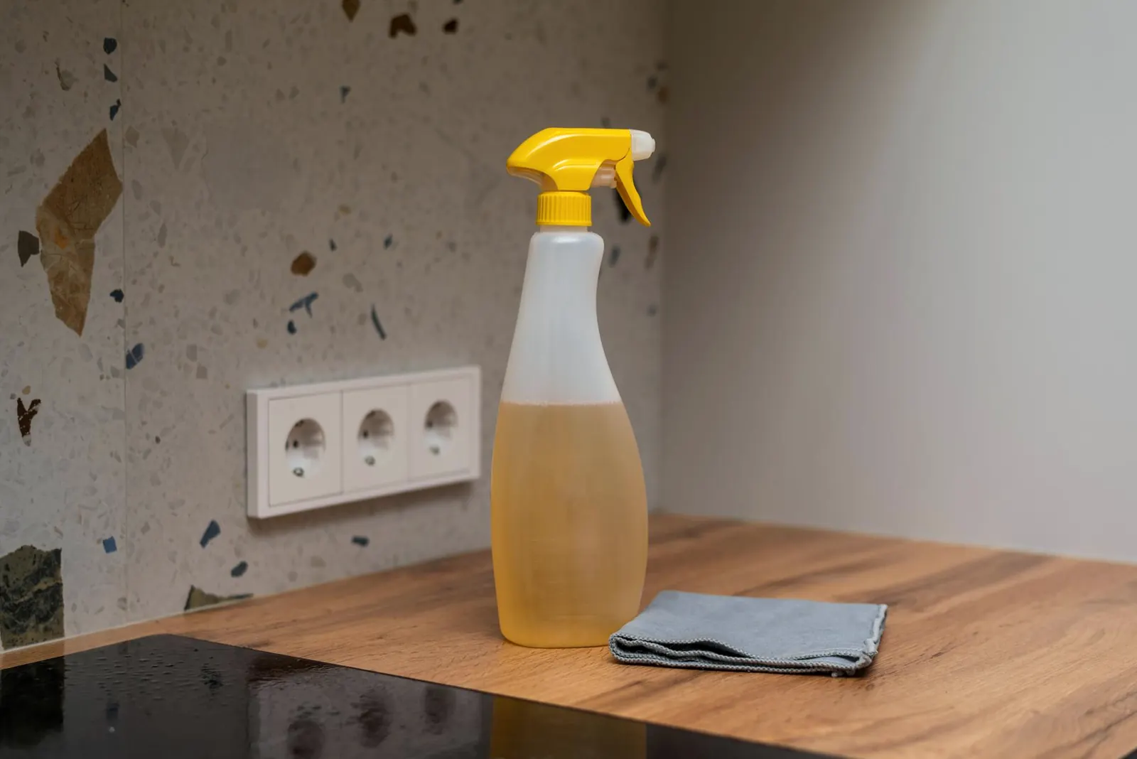 A spray bottle of cleaning liquid and a folded cloth on a wooden worktop